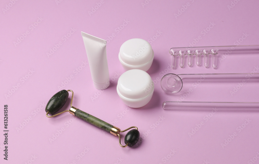Acne treatment. Nozzles for local darsonvalization, jade roller, cream tube and jar on a purple background. Beauty concept. Acne treatment. Nozzles for local darsonvalization, jade roller, cream tube and jar on a purple background. Beauty concept.
