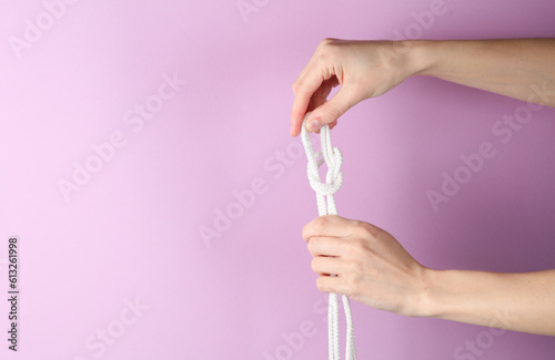 Women's hands knit a rope knot on a purple background. Leisure