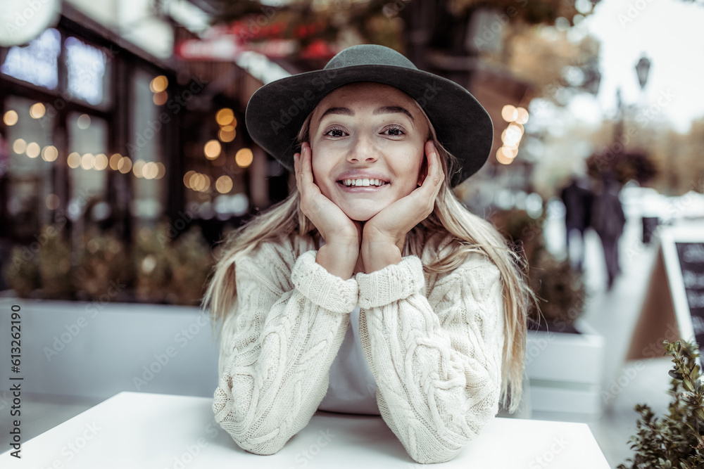 Young smiling cute woman in hat sitting at table in outdoor cafe. Lifestyle Young smiling cute woman in hat sitting at table in outdoor cafe. Lifestyle