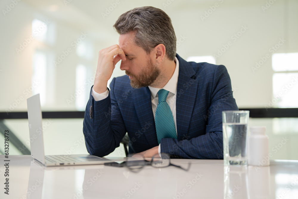 Headache, tiredness and stress. Business man in suit uses a laptop, is tired got headache migraine. Headache pain concept. Painful men are stressed at work in office. Stressful and headache.