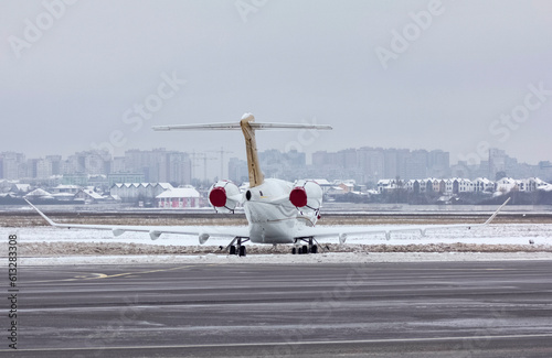 Private white business jet jet stands at the airport under the snow in winter against a cloudy sky 