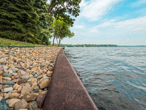 Surface level view of a metal retaining wall dividing the lake from the land. An ornamental stone path runs along the retaining wall. A retaining wall is used to protect land from soil erosion.