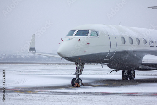 
Private white business jet jet stands at the airport under the snow in winter against a cloudy sky close-up