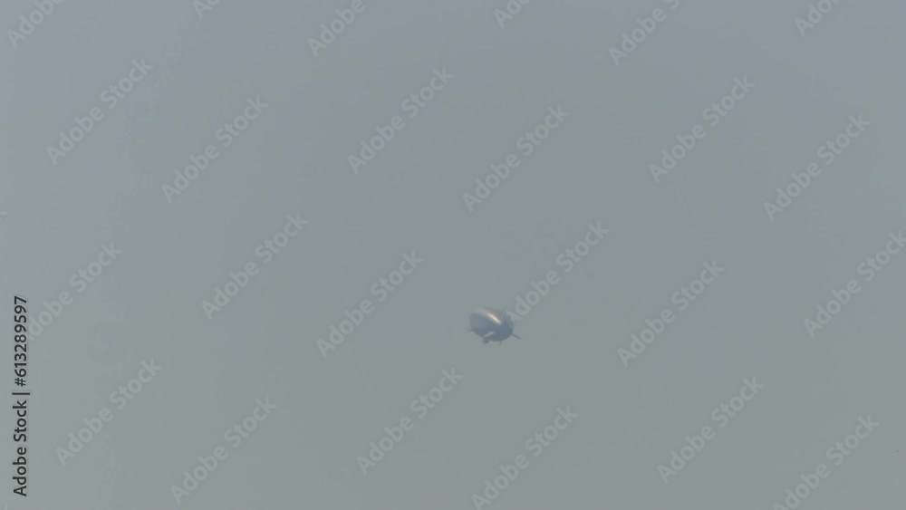 View with airship powered by helium - flight on the background of hazy gray sky. View on sunny and misty morning.
