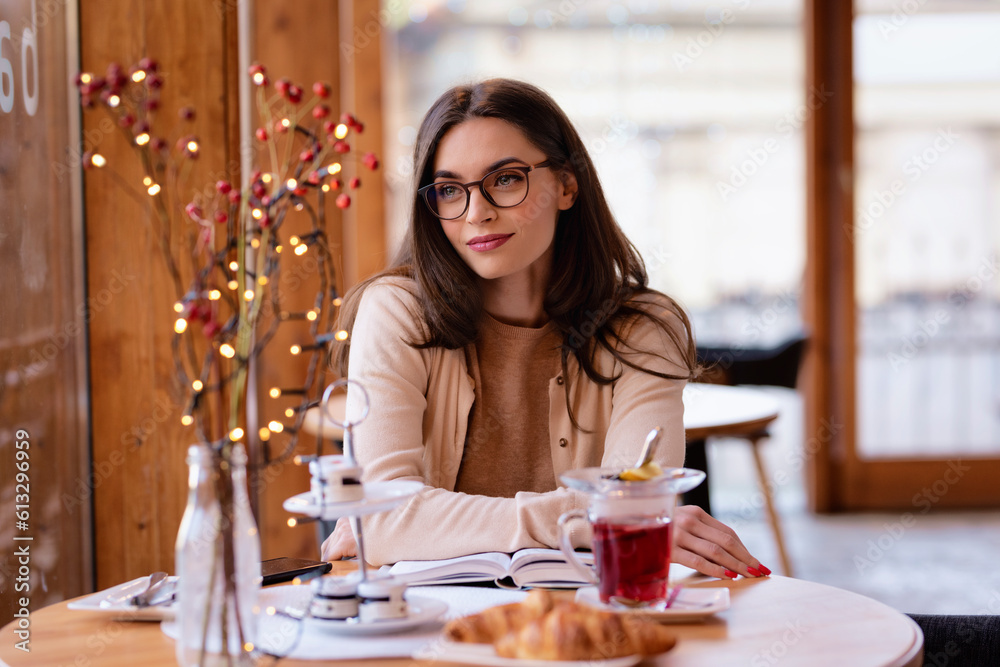 Attractive brunette haired woman sitting in a cafe next to window and daydreaming
