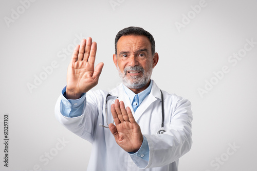 Unhappy caucasian mature man doctor in white coat making stop gesture with hands © Prostock-studio