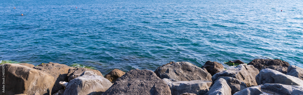 Fototapeta premium Tranquility rocky beach with big black stones, blue sea and sky as background, tranquil and looks beautiful.Big stone beach in front of sea with sky