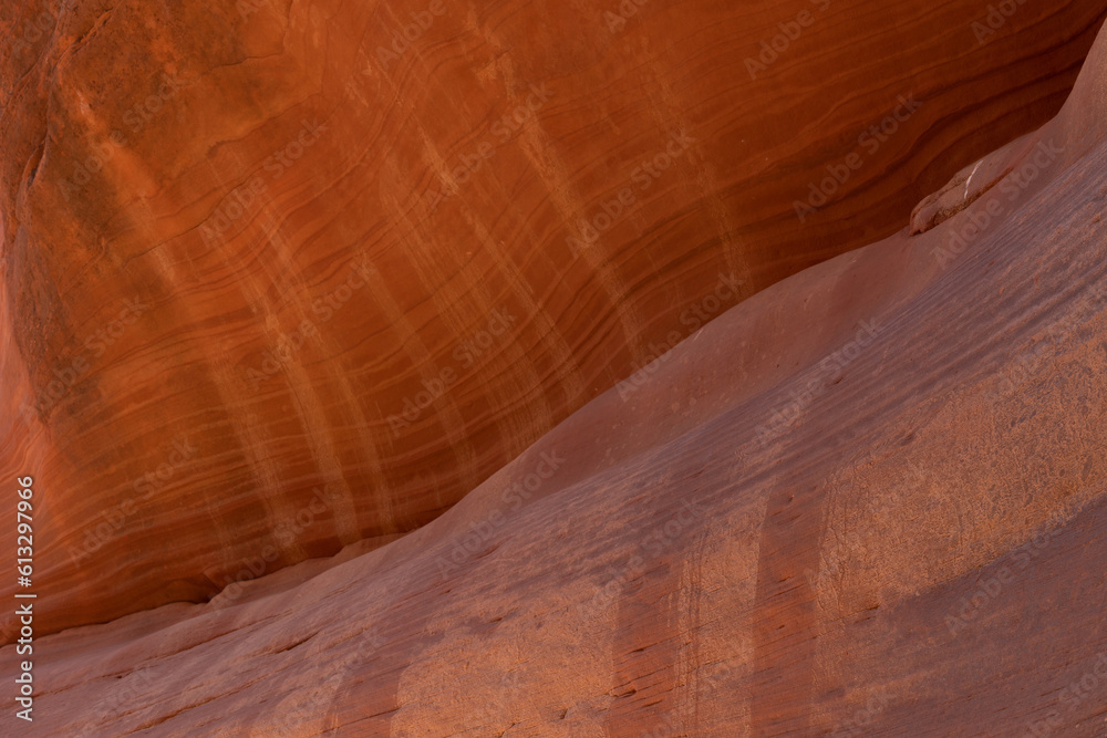 The face of a red sandstone cliff in Peekaboo Canyon, Utah is streaked with horizontal sedimentary lines and vertical oxidized lines where water has run down the cliff during rain storms.
