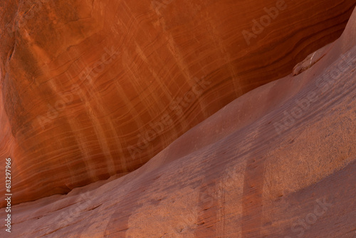 The face of a red sandstone cliff in Peekaboo Canyon, Utah is streaked with horizontal sedimentary lines and vertical oxidized lines where water has run down the cliff during rain storms.