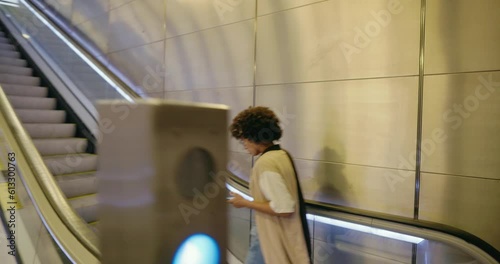 A beautiful black girl in the subway goes up the escalator and chats on her smartphone. A young woman with a smartphone in her hands climbs the escalator and smiles. African American on the subway.