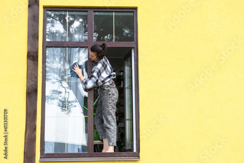 Wallpaper Mural A woman manually washes the window of the house with a rag with a spray cleaner and a mop outside. Safety at height, restoring order and cleanliness in the spring, cleaning service Torontodigital.ca