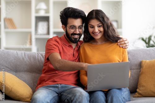 Young Indian Couple With Laptop Booking Vacation Online While Relaxing At Home