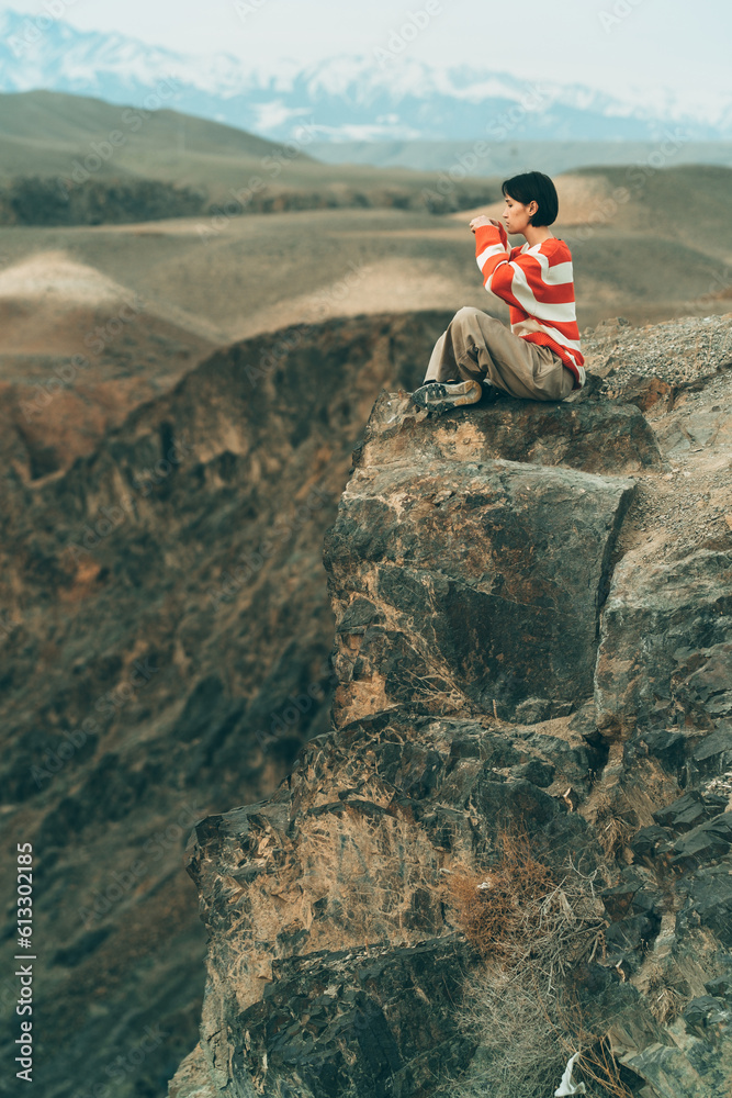A girl in a striped sweater taking photos on smartphone sitting on a cliff