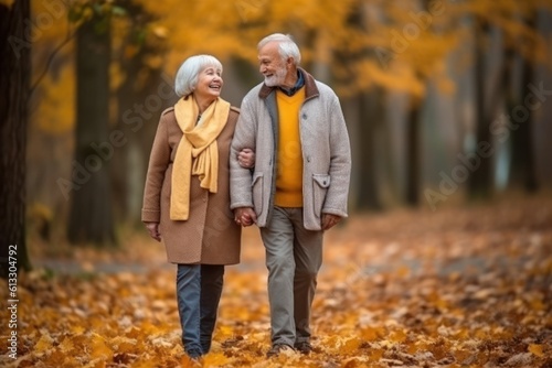 Happy senior man and woman walking on scattered yellowed leaves in scenic autumn park