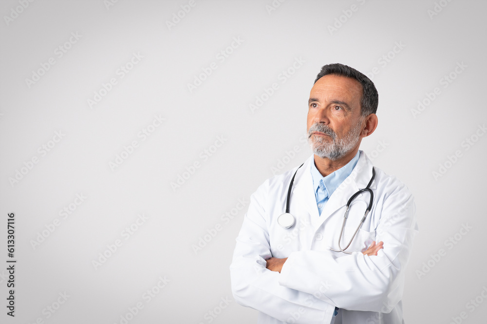 Serious confident caucasian senior doctor therapist in white coat with crossed arms looking at copy space Serious confident caucasian senior doctor therapist in white coat with crossed arms looking at copy space