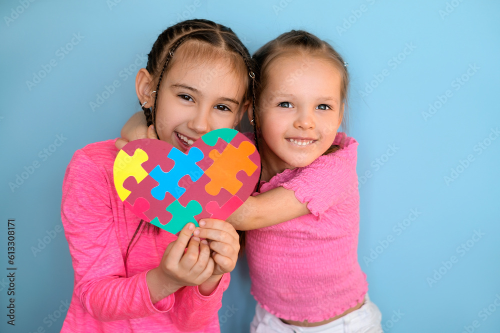 Two happy cheerful sisters show the symbol of autism with the image of colored puzzles Two happy cheerful sisters show the symbol of autism with the image of colored puzzles