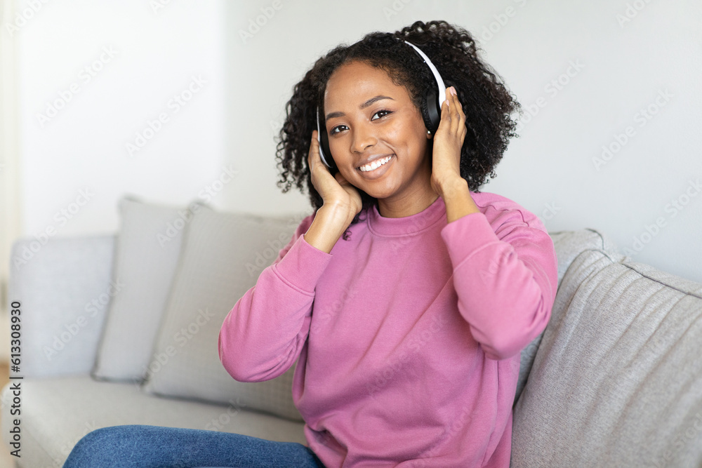 Cheerful millennial black woman in wireless headphones relax, enjoy free time, listen music, lesson, sit on sofa Cheerful millennial black woman in wireless headphones relax, enjoy free time, listen music, lesson, sit on sofa