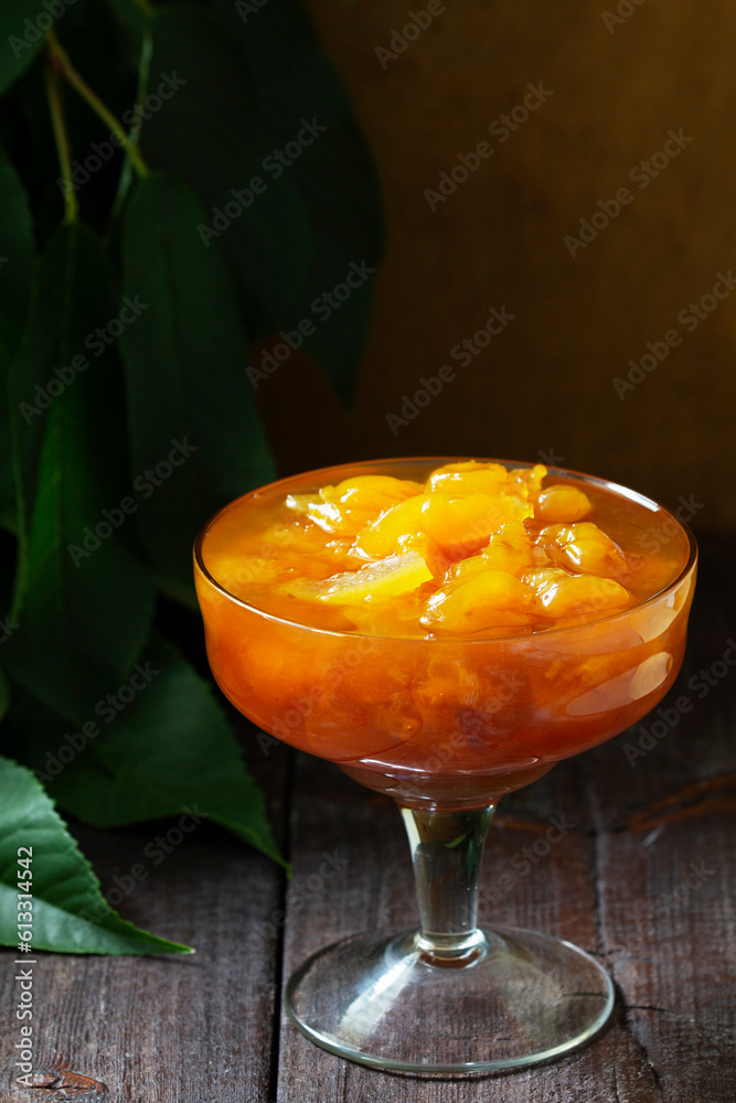 Yellow cherry jam with lemon and vanilla in a glass bowl on a wooden background.