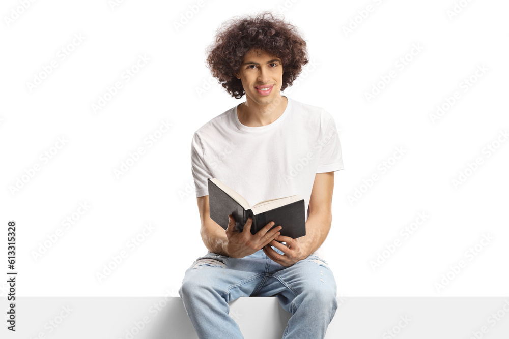 Young man with curly hair sitting on a panel and holding a book Young man with curly hair sitting on a panel and holding a book