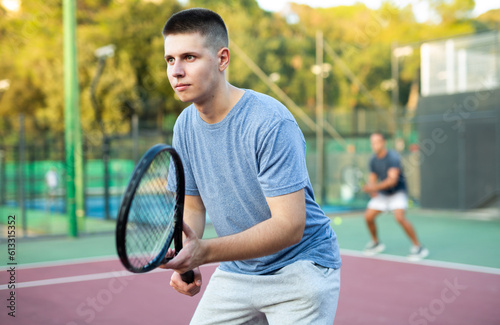 Young man in shorts and t-shirt playing tennis on court. Racket sport training outdoors. © JackF