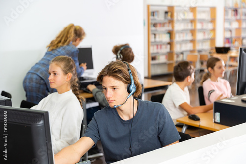 Portrait of a concentrated fifteen-year-old schoolboy studying at a computer wearing headphones in class at lesson