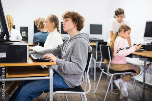 Teenager girls and boys studying in computer lab during lesson.