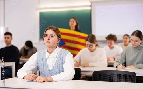 Students study in classroom, teacher stands behind with flag of Catalonia