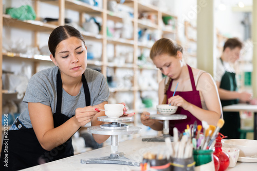 Young woman teacher in apron makes ceramic cup in ceramic workshop