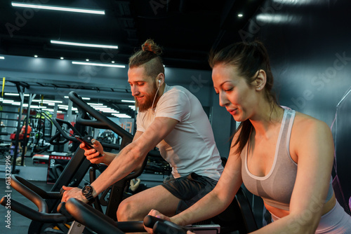 A young, handsome man works out during a spinning session on a cycling machine at the gym with his friends. 