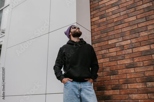 City portrait of handsome hipster guy with beard wearing black blank hoodie or sweatshirt with space for your logo or design. Mockup for print