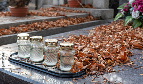 Old burned candles in autumn on graves covered with yellow leaves. Cleaning the graves before the Day of the Dead.