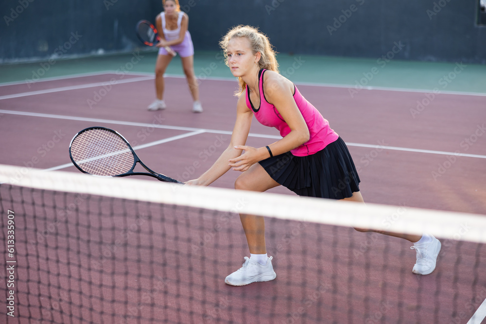 Positive attractive female player hits ball close to net while playing tennis