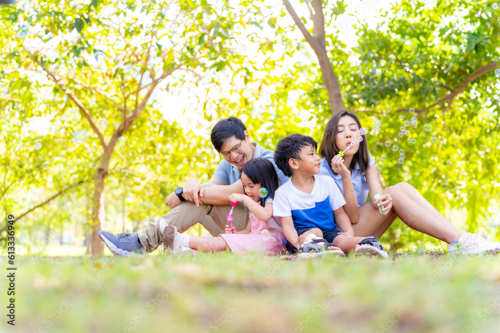 Fototapeta premium Happy Asian family enjoy and fun outdoor activity lifestyle on summer holiday vacation. Parent and little child playing bubble wand together at public park in the city. Family relationship concept.