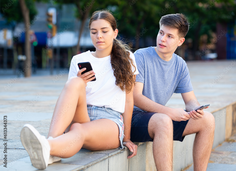 Two young people with mobile phones are sitting on the step