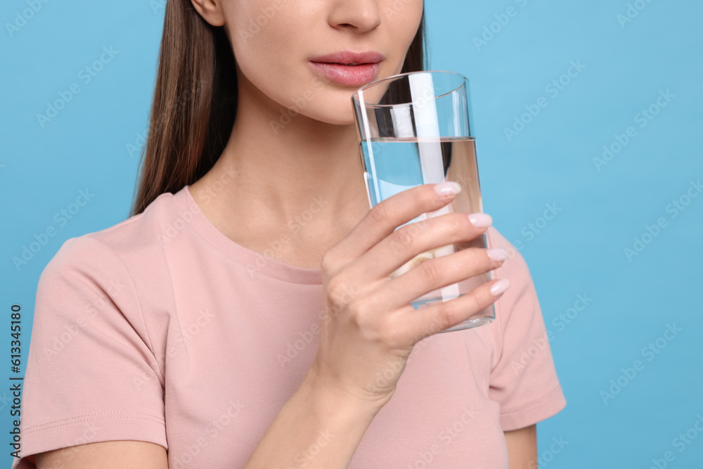 Healthy habit. Woman drinking fresh water from glass on light blue background, closeup Healthy habit. Woman drinking fresh water from glass on light blue background, closeup