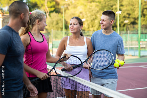 Group of four tennis players standing on court and talking friendly about match