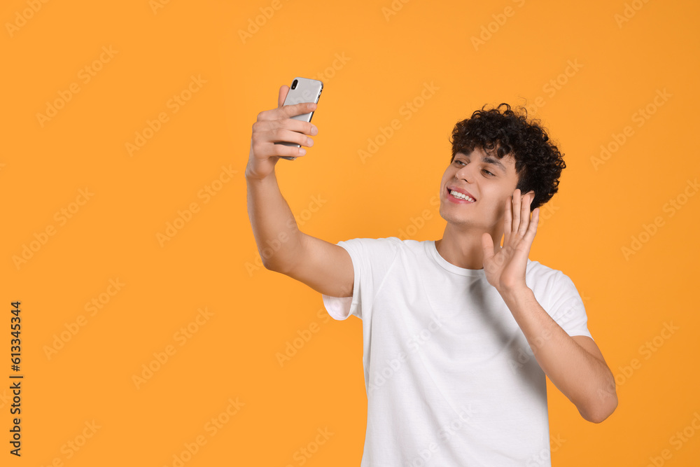 Handsome young man having video chat on smartphone against orange background. Space for text Handsome young man having video chat on smartphone against orange background. Space for text