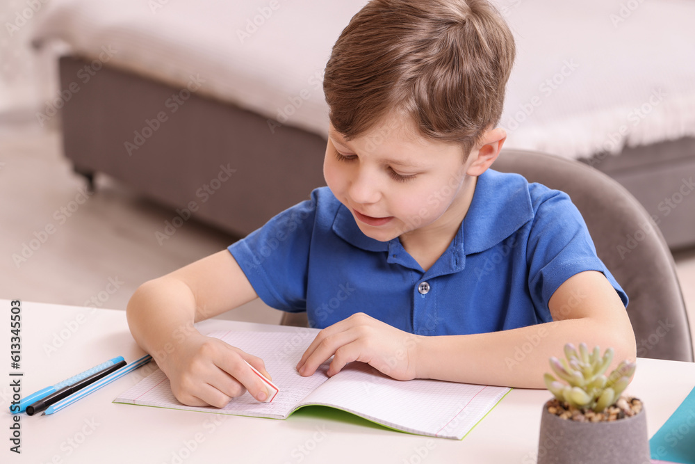 Little boy erasing mistake in his notebook at white desk indoors Little boy erasing mistake in his notebook at white desk indoors