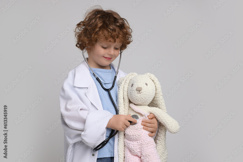 Little boy playing doctor with toy bunny on light grey background Little boy playing doctor with toy bunny on light grey background