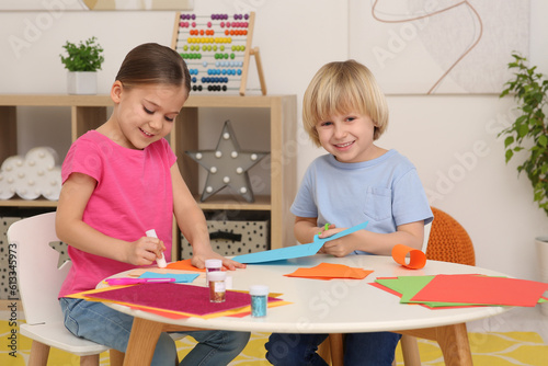 Girl using glue stick and boy cutting paper at desk in room. Home workplace