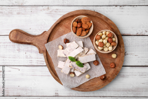 Pieces of delicious nutty nougat on white wooden table, top view