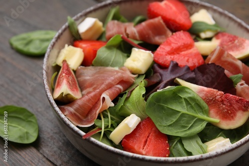 Tasty salad with brie cheese, prosciutto, strawberries and figs on table, closeup