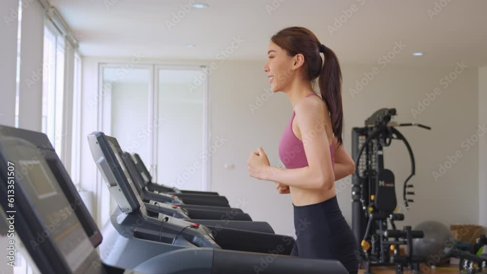 Asian young sportswoman exercise by running on treadmill in gym club.