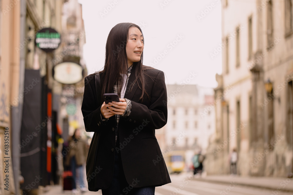 Young busy successful beautiful Asian business woman, korean professional businesswoman holding cellphone using smartphone standing or walking on old city street outside. Young busy successful beautiful Asian business woman, korean professional businesswoman holding cellphone using smartphone standing or walking on old city street outside.