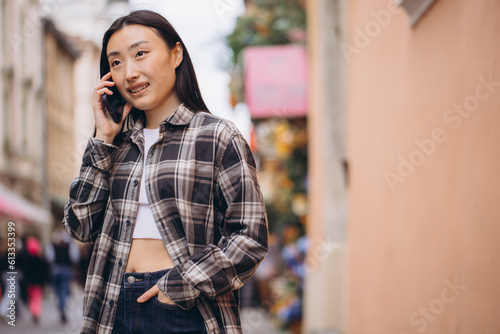 Portrait of a beautiful Korean woman on the old town street. Asian woman in casual clothes talking on the phone, modern technology and lifestyle.