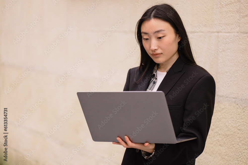 Portrait of a beautiful brunette Korean woman with a laptop. Asian business lady in a suit uses modern technology. Portrait of a beautiful brunette Korean woman with a laptop. Asian business lady in a suit uses modern technology.