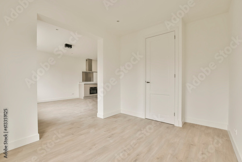 an empty living room with white walls and wood flooring  there is a kitchen in the wall to the right