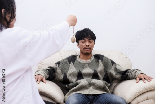 Fotografie Female psychiatrist hypnotizing patient sitting on sofa using pendulum during hy