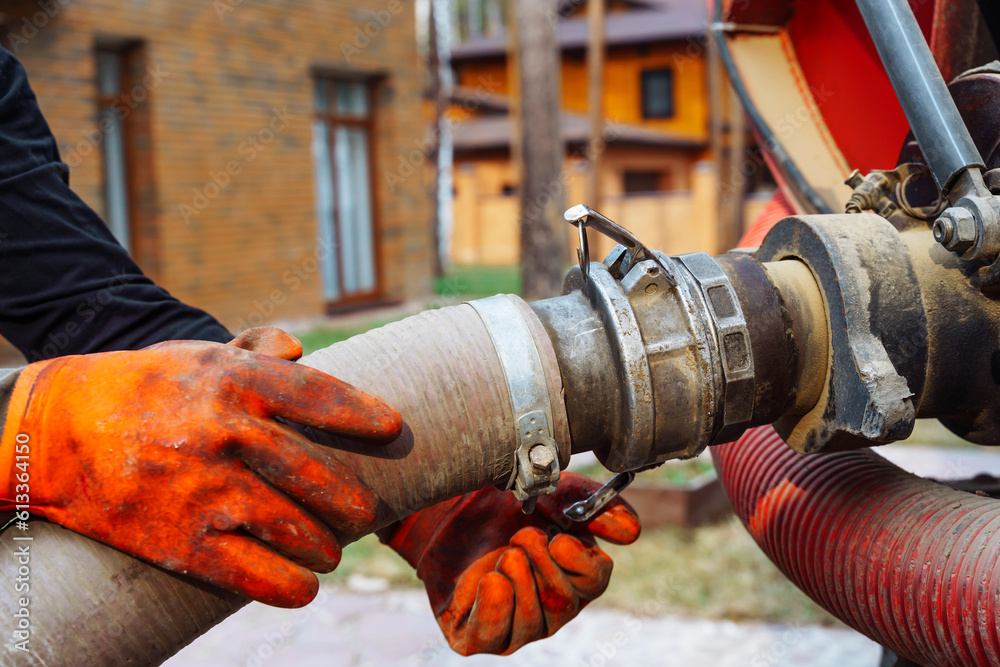 a hand connects a suction hose to a sewage tanker truck. Sewer pumping