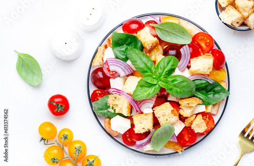 Panzanella italian vegetable salad with stale bread, colorful tomatoes, mozzarella cheese, onion, olive oil, salt and green basil, white table background, top view